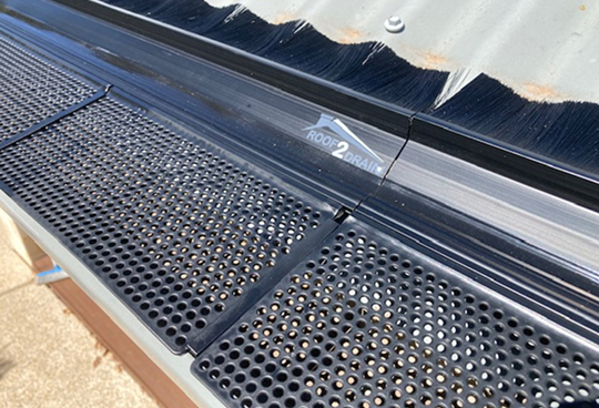 A metal roof vent topped with a black metal mesh gutter guard cover with holes for effective debris and pests protection made by Roof2Drain